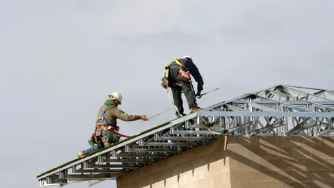 Workers installing a commercial metal roof on a high-rise building in New York City, using safety harnesses and professional equipment.