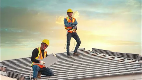 Two construction workers installing roof panels while wearing safety gear.
